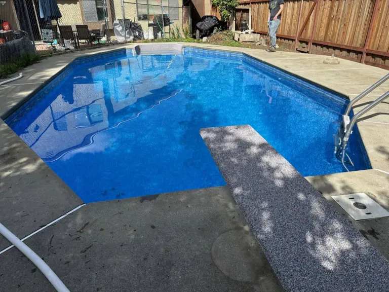 Blue pool with a diving board and stainless ladder on an aggregate concrete deck