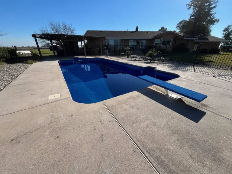 Pool with a deep blue liner and a diving board, a pergola and patio behind
