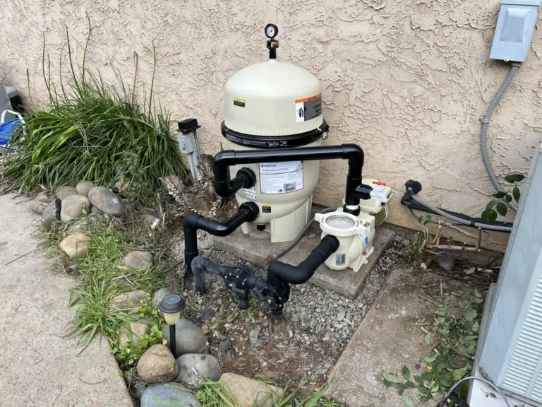 Pool equipment pad: a filter and pump plumbed in black PVC beside a stucco wall