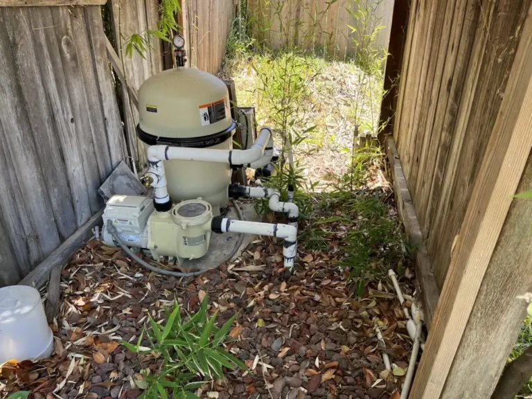 Filter and pump tucked into a narrow side yard between wooden fences