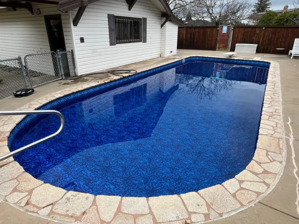 Long pool with a deep blue liner, a stainless handrail and a flagstone deck beside a white house