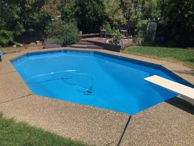 Bright blue freeform pool with a diving board, edged by an aggregate deck and green lawn