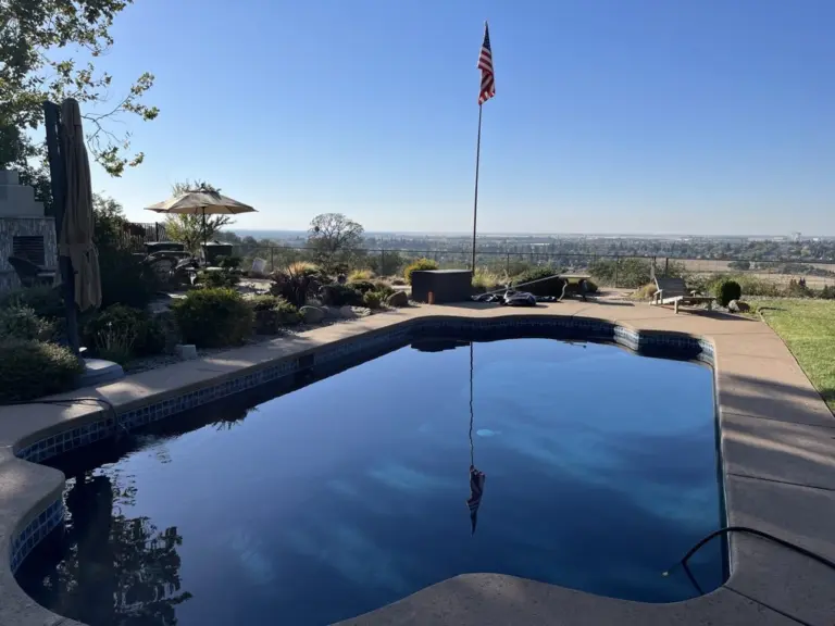 Hillside pool with dark water reflecting the sky, a flag and a valley view beyond