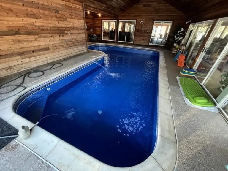 Indoor pool in a wood-paneled pool house, a deep blue liner and a light deck