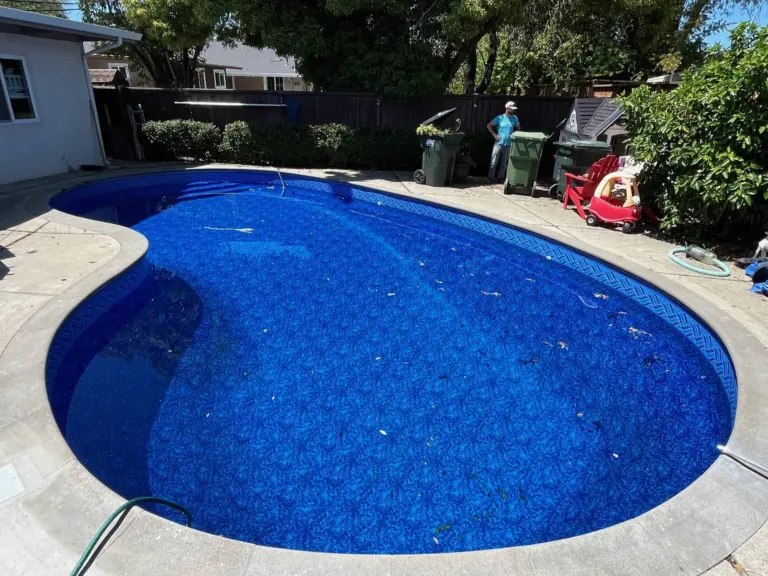 Kidney-shaped pool with a deep blue patterned liner and a light concrete deck