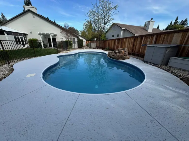 Kidney-shaped pool with a new vinyl liner, set in a wide white concrete deck beside a house with a pergola