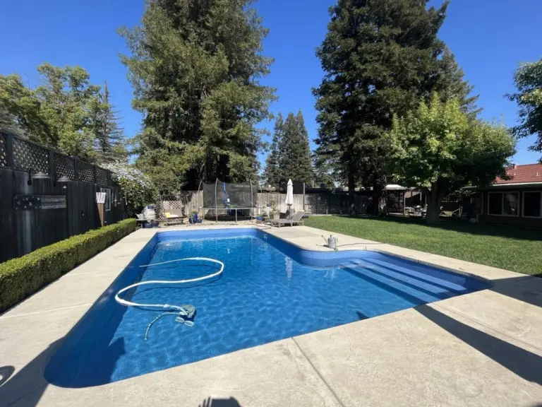 Long pool with a light blue liner and steps across the shallow end, tall trees behind