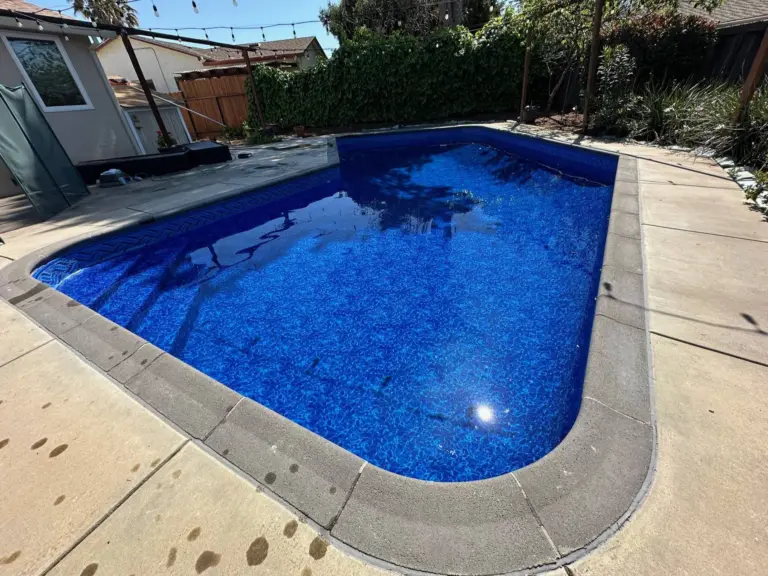 Rectangular pool with a deep blue mosaic-pattern liner and gray concrete coping