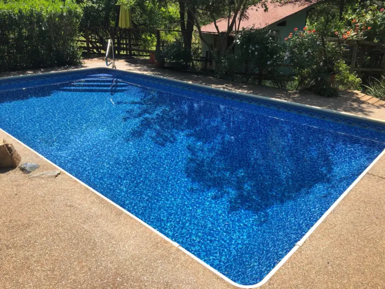 Rectangular pool with a blue mosaic-pattern liner and corner steps, shaded by tall trees