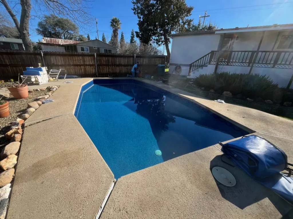 Pool with a navy liner beside a concrete deck, an automatic pool cleaner resting on the edge
