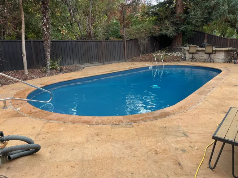 Oval pool with clear blue water on a tan concrete deck surrounded by trees