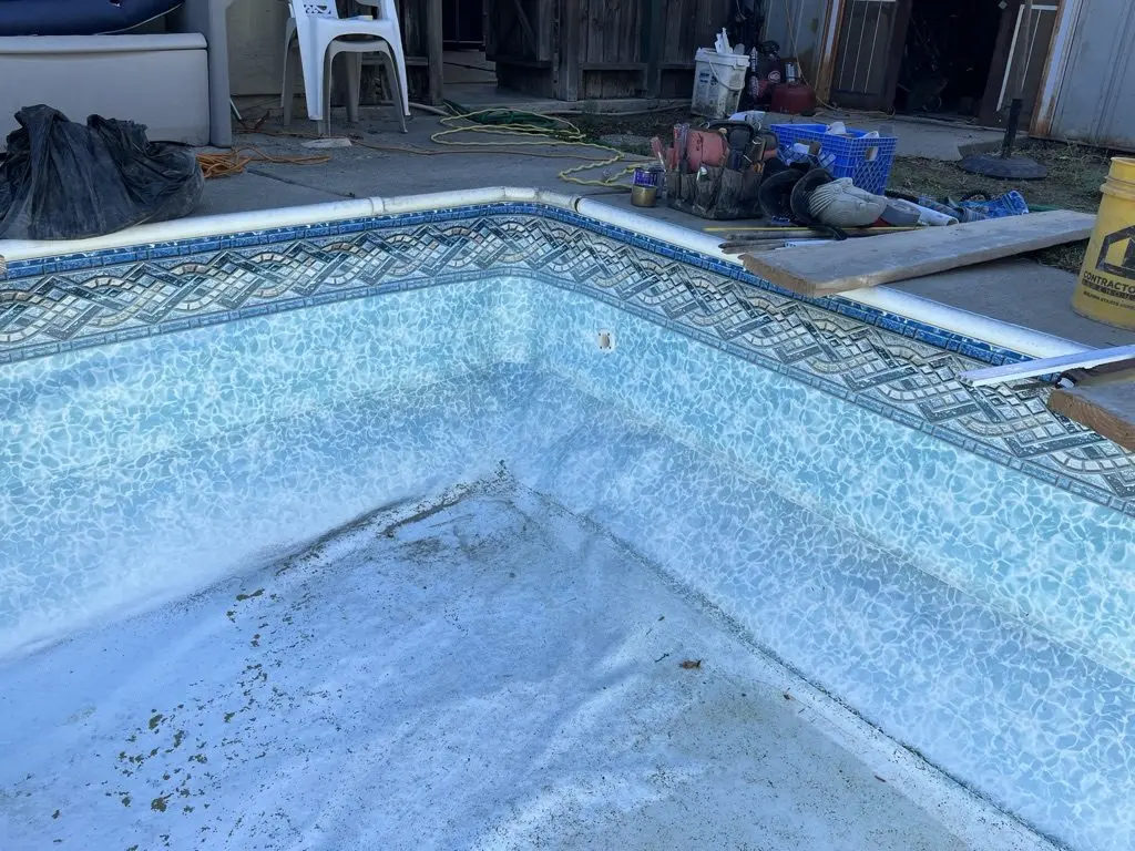 Project 1, start: the old liner with its diamond border in the drained pool, mesh cover folded on the deck