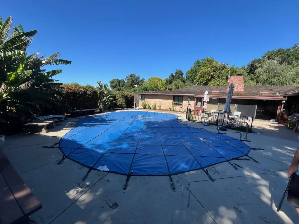 Blue mesh safety cover stretched tight over a backyard pool on a sunny day