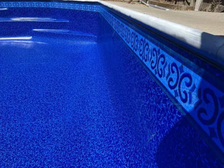 Pool wall with a scroll-pattern tile border just under the coping, deep blue water below