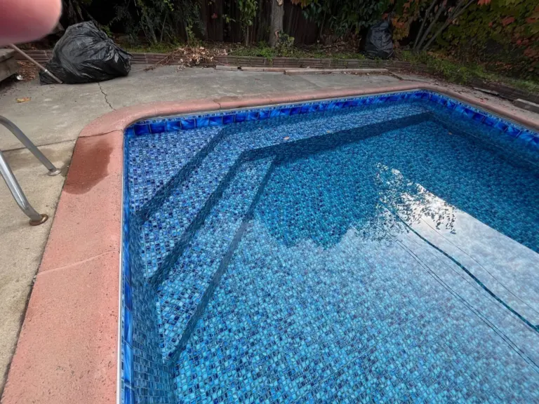 Shallow-end steps in a pool with a blue mosaic liner and a red-toned deck