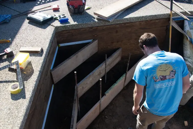 A crew member in a Rustic Pools sun-logo shirt checking the step forms