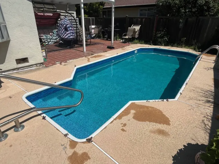Freeform pool with turquoise water, two handrails and a concrete deck