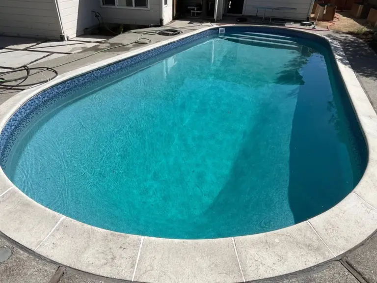 Oval pool with turquoise water, a mosaic tile border and a light concrete deck