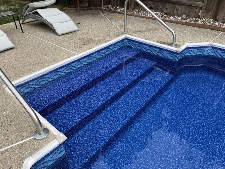 Wide vinyl-covered steps with a stainless handrail in a pool with a wave tile border