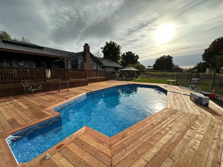 L-shaped pool with a blue vinyl liner framed by a new wood deck, the sun breaking through clouds over the yard